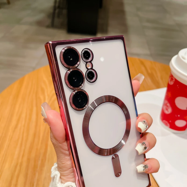 A person's hand with decorated nails holding a maroon and silver smartphone with multiple camera lenses, above a white saucer and a red cup with a dotted design in a café setting.