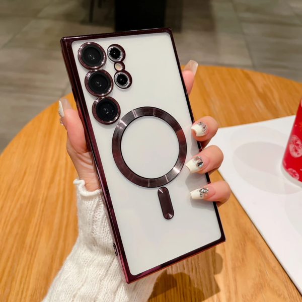 A hand with decorative nail art holds a modern smartphone with a distinctive arrangement of multiple camera lenses and a metallic ring accent. The setting appears to be a cafe table with a drink in the background.