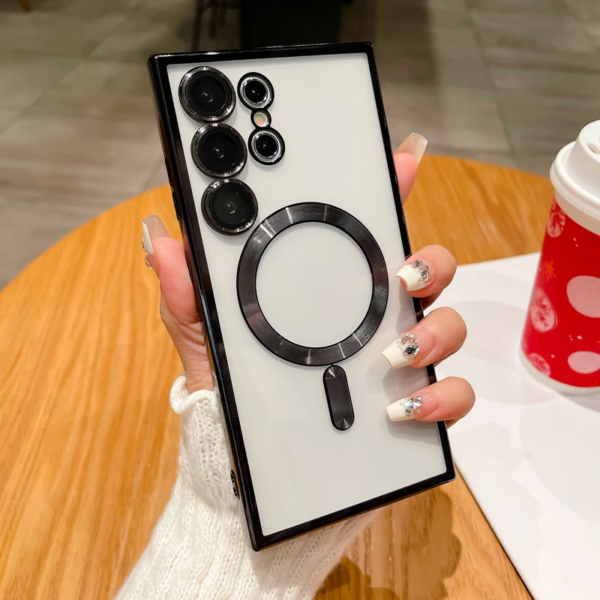 A person holding a smartphone with multiple camera lenses and a graphical illustration of a magnifying glass on its screen, next to a red cup with white snowflakes on a white saucer.