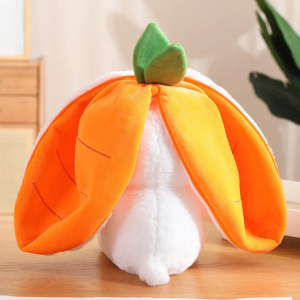 A plush toy resembling the backside of a white rabbit with large, orange carrot-like ears and a green top, sitting on a wooden surface against a soft-focused indoor background.