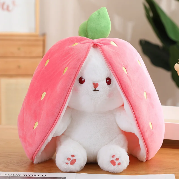 A plush toy rabbit with a strawberry cape, featuring white fur, red eyes, a cute nose, and paw prints, seated on a table.