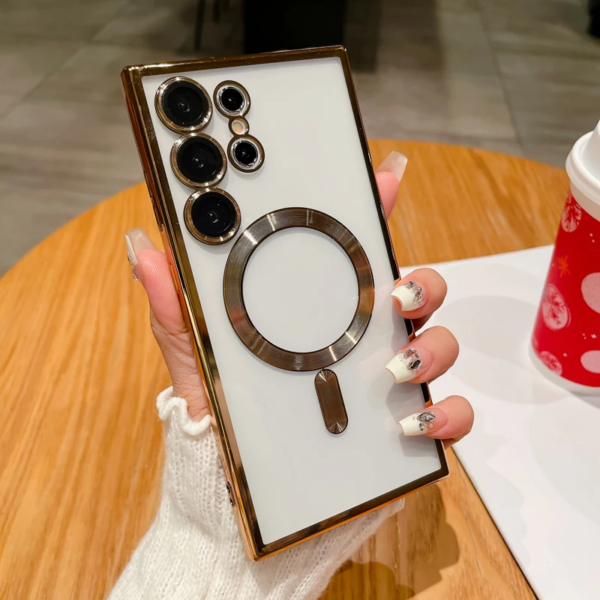 A person holding a white smartphone with an unusual rear camera setup and a large circular design element, against a background featuring a table with a red cup adorned with snowflake patterns. The person has long, manicured nails with a floral design.