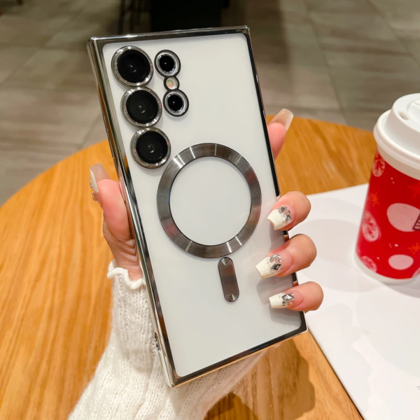 A person's hand with a manicure holding a modern smartphone with multiple camera lenses and a distinctive circular design on the back, with a red cup featuring festive decorations in the background.