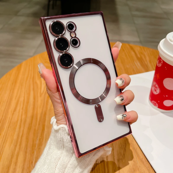 A person holding a smartphone with a distinctive camera module, featuring multiple lenses and a ring-like attachment on the back, displayed against a coffee table with a cup visible in the background. The person's nails are manicured with decorative nail art.
