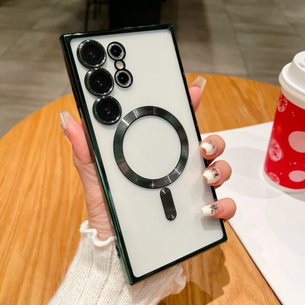 A person's hand with pink nail art holding a smartphone with a distinctive circular camera module and magnetic ring accessory on its back, resting on a white surface next to a festive red cup.